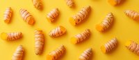 Fresh turmeric roots scattered on bright yellow background, raw organic rhizomes with natural pattern layout showing culinary and wellness ingredients.