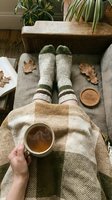 Cozy autumn hygge scene with wool socks, hot tea cup, plaid blanket, and dry oak leaves on a sofa, top view.