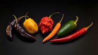Assorted hot chili peppers variety including dried, fresh red, yellow, orange and green peppers arranged on dark background for culinary spice cooking.
