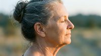 Senior woman with gray hair in bun, peaceful expression, outdoor natural light, contemplative portrait for wellness and aging themes.