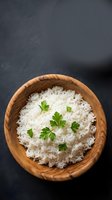 Cooked white rice with fresh parsley garnish served in wooden bowl on dark slate background for healthy meal preparation and cooking concepts.