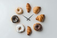 Assorted donuts and croissants arranged as a clock on a white background, representing breakfast time, bakery concept, and morning food routine.