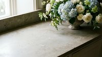 Elegant stone countertop near a window with a vintage vase of blue hydrangeas and white roses, soft natural light, copy space.