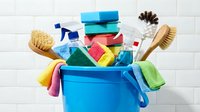 Blue cleaning bucket filled with colorful household supplies including sponges, brushes, spray bottles and cloths for spring cleaning and maintenance.