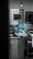 Male hand holding digital network visualization with kitchen appliances blurred in background, representing smart home technology, IoT connectivity, and intelligent kitchen automation systems.