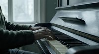 Hands playing piano keys in moody lighting with sheet music, musician practicing classical instrument indoors for music education and artistic expression.