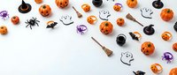 Halloween decorations scattered on white background with pumpkins, ghosts, spiders, witches hats and brooms creating festive autumn holiday pattern.