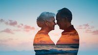 Romantic double exposure silhouette of senior interracial couple merged with vibrant sunset ocean scene, showing intimate moment against pink and orange sky.