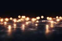 Glowing fairy lights creating magical bokeh effect on dark surface with reflections, warm golden illumination for festive holiday atmosphere and decor.