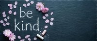 Be kind chalk lettering on dark slate board surrounded by pink cherry blossom petals, motivational kindness message for cards and social media.