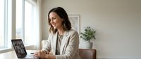 Professional businesswoman smiling during video conference call on laptop in modern office workspace for remote work and virtual meetings.
