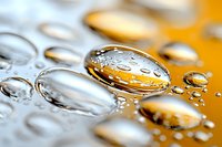 Macro photography of pure water drops on reflective surface with orange background creating abstract pattern of spherical droplets and light refraction effects.