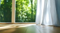 Sunlight streaming through window with white curtains onto wooden floor, creating warm atmosphere in peaceful room with forest view.