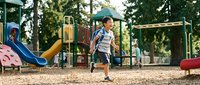 Young Asian boy running and playing at colorful outdoor playground equipment during sunny day. Active childhood recreation and exercise concept.