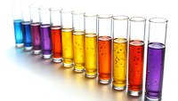 Row of colorful liquid-filled test tubes showing gradient from blue through yellow and red to purple, with bubbles rising in transparent glass containers.