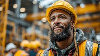 Smiling African American construction worker in safety gear at industrial site with warm lighting and blurred warehouse background for workplace safety concepts.