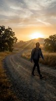 Woman jogging on rural dirt road at golden hour sunrise with dramatic sky, mountains and trees. Fitness and outdoor exercise concept.