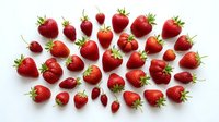 Fresh ripe strawberries scattered on white background. Organic red berries with green leaves isolated for healthy food design and culinary projects.