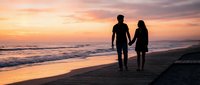 Romantic couple silhouettes walking hand in hand on beach at sunset with golden sky and ocean waves for love and relationship concepts.