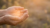 Open cupped hands catching warm golden sunlight with soft bokeh background creating peaceful spiritual moment for meditation and mindfulness concepts.