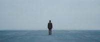 Lone businessman standing on calm ocean surface under overcast sky, surreal conceptual scene representing solitude, contemplation, and infinite possibilities.