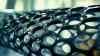 Macro view of dark metallic mesh structure with circular holes creating abstract industrial pattern, suitable for technology or engineering backgrounds.