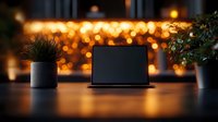 Laptop on wooden desk with bokeh lights background and decorative plants in modern workspace setting creates cozy evening atmosphere.
