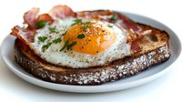 Fried egg on dark rye bread with crispy bacon and fresh herbs served on white plate for breakfast menu design and food photography projects.