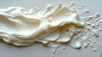 Creamy white liquid splash frozen in motion with dynamic waves and droplets creating abstract flowing shapes against light background. Suitable for dairy advertising.
