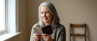 Mature Caucasian woman with gray hair enjoying reading book by window in cozy home interior, peaceful retirement lifestyle and leisure activities.