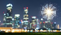 Sparkler burning bright against blurred city skyline at night creating magical bokeh lights and festive atmosphere for celebrations and holidays.