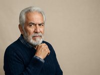 Senior man with gray hair and beard wearing dark sweater, hand near chin in thoughtful pose against neutral background. Suitable for healthcare, business, and lifestyle projects.