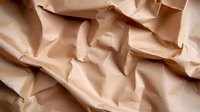 Crumpled beige paper background with natural folds and wrinkles creating abstract textural pattern with light and shadow play. Suitable for design projects.