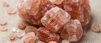Himalayan salt crystals and chunks scattered on neutral fabric surface, showcasing natural mineral texture and warm peachy tones for wellness, spa, and culinary content.