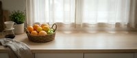 Wicker basket filled with fresh oranges and lemons on wooden kitchen counter near window with sheer curtains, bright natural light, home interior styling.