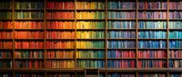 Colorful rainbow bookshelf wall with thousands of books arranged by color spectrum from red to blue creating vibrant library display for education and reading.