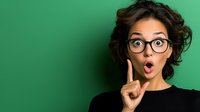 Young Hispanic woman with glasses showing surprised expression, raised finger against green background, wearing black top. For advertising and social media content.