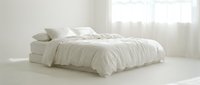 Unmade bed with white crumpled bedding, pillows and sheets in bright minimalist bedroom with natural light from window, suitable for home decor and lifestyle content.