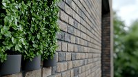 Fresh green plants in modern black planters mounted on textured brick wall creating contemporary outdoor garden design element with geometric pattern.