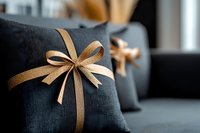 Elegant dark gray decorative pillow adorned with golden ribbon bow on sofa, modern home decor detail creating cozy atmosphere for living room interior design.