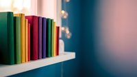 Colorful books arranged on white shelf with warm bokeh lights creating cozy reading atmosphere for home library and education concepts.
