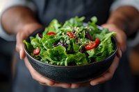Fresh mixed green salad with cherry tomatoes and seeds in dark bowl held by hands. Healthy eating concept for restaurant menu design.