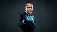 Mature male professional in dark business suit holding glowing zero percent neon sign, representing interest rates, finance, and banking concepts for commercial use.