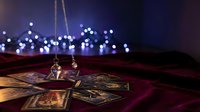 Mystical tarot cards spread on burgundy velvet with golden pendulum and soft bokeh lights creating magical fortune telling atmosphere for spiritual guidance.