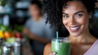 Young African American woman with curly hair smiling while holding fresh green smoothie at cafe. Healthy lifestyle and wellness concept focused on nutritious beverages.