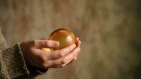 Hands gently holding glowing golden orb of light with warm magical energy radiating soft illumination against blurred background for spiritual concepts.