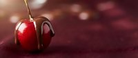 Fresh red cherry with melted chocolate dripping on dark burgundy surface with warm bokeh lights creating romantic dessert atmosphere for culinary designs.