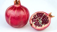 Fresh ripe pomegranate whole and cut in half showing juicy red seeds and white membrane on white background, healthy organic fruit for food design.