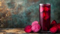 Fresh beetroot juice in tall glass with sliced beets on rustic wooden table against blurred background for healthy lifestyle and nutrition concepts.