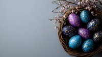 Cosmic galaxy-inspired Easter eggs decorated in blue, purple and gold speckles nestled in woven basket with cherry blossom branches on gray background.